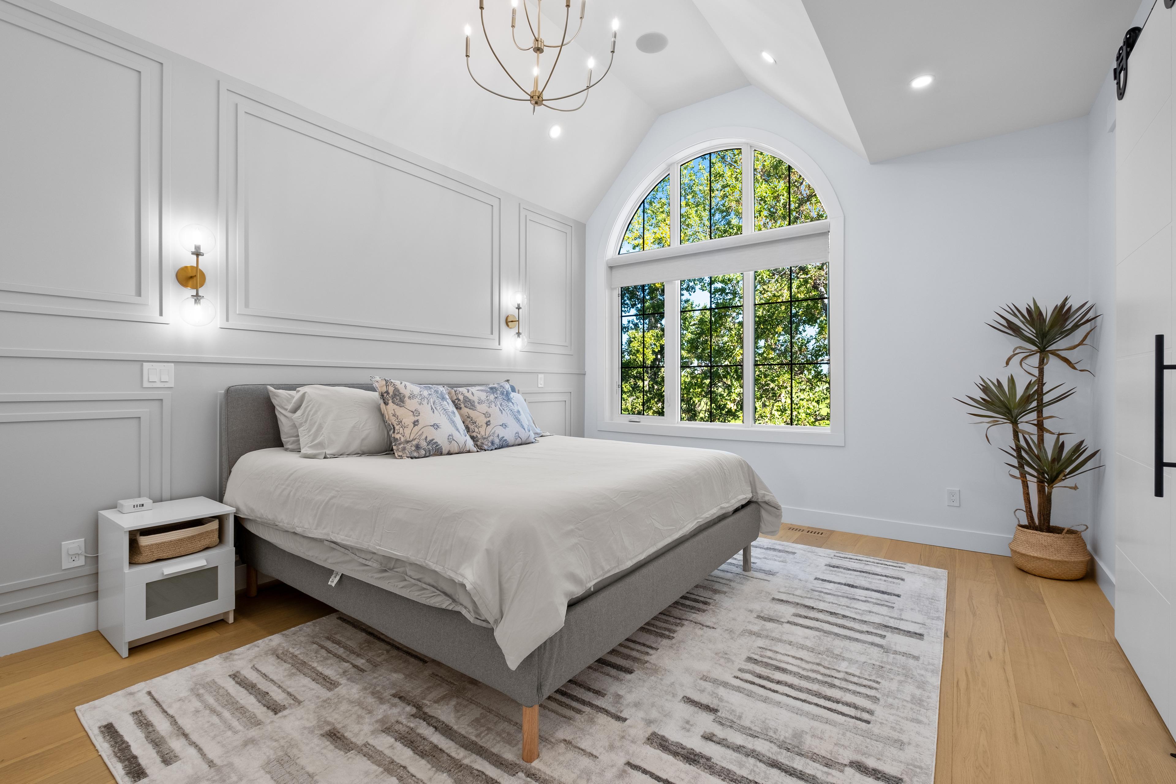 Primary bedroom with a vaulted ceiling, arched window and panelled walls