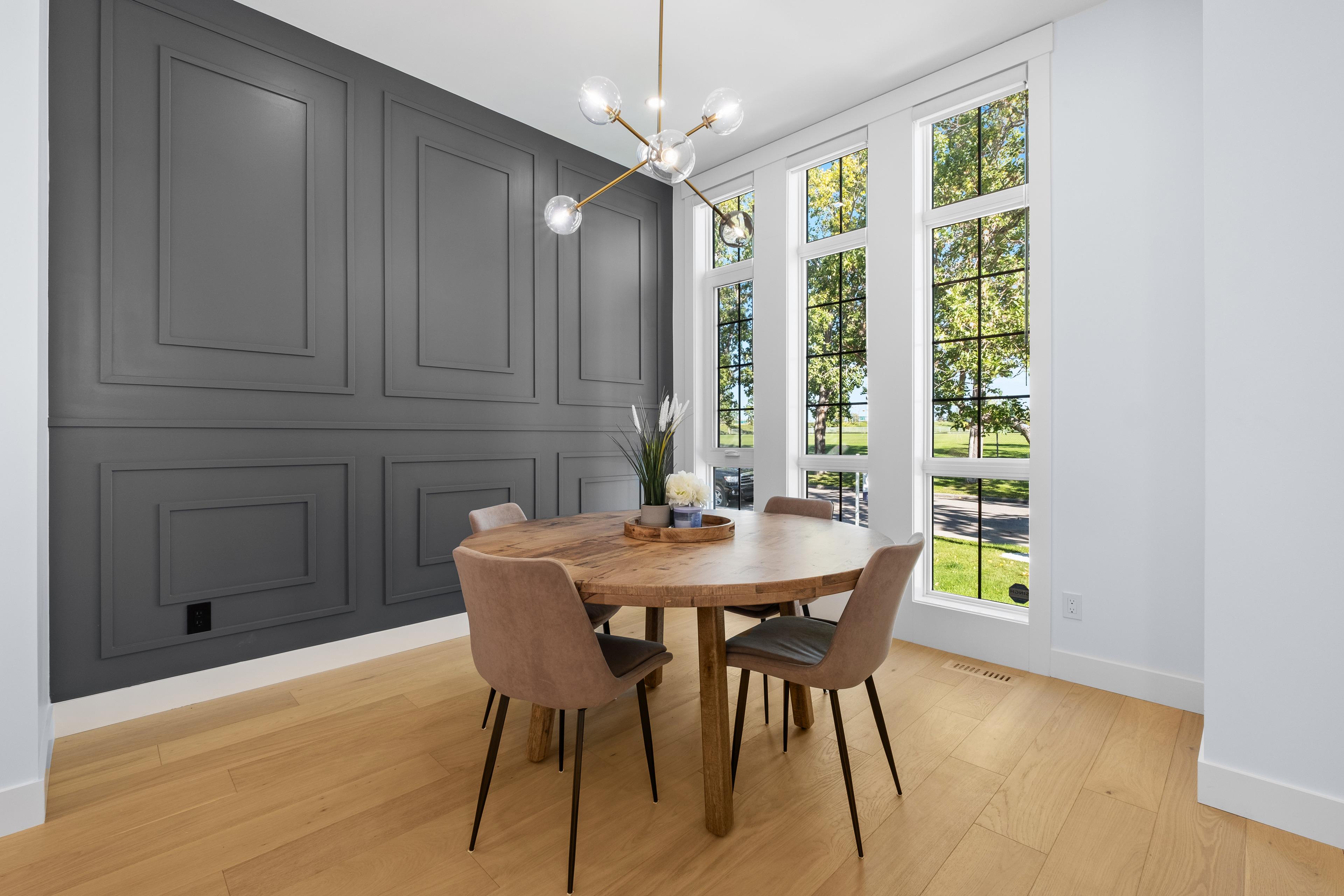 Dining room with a dark panelled feature wall, round wood table and tall windows