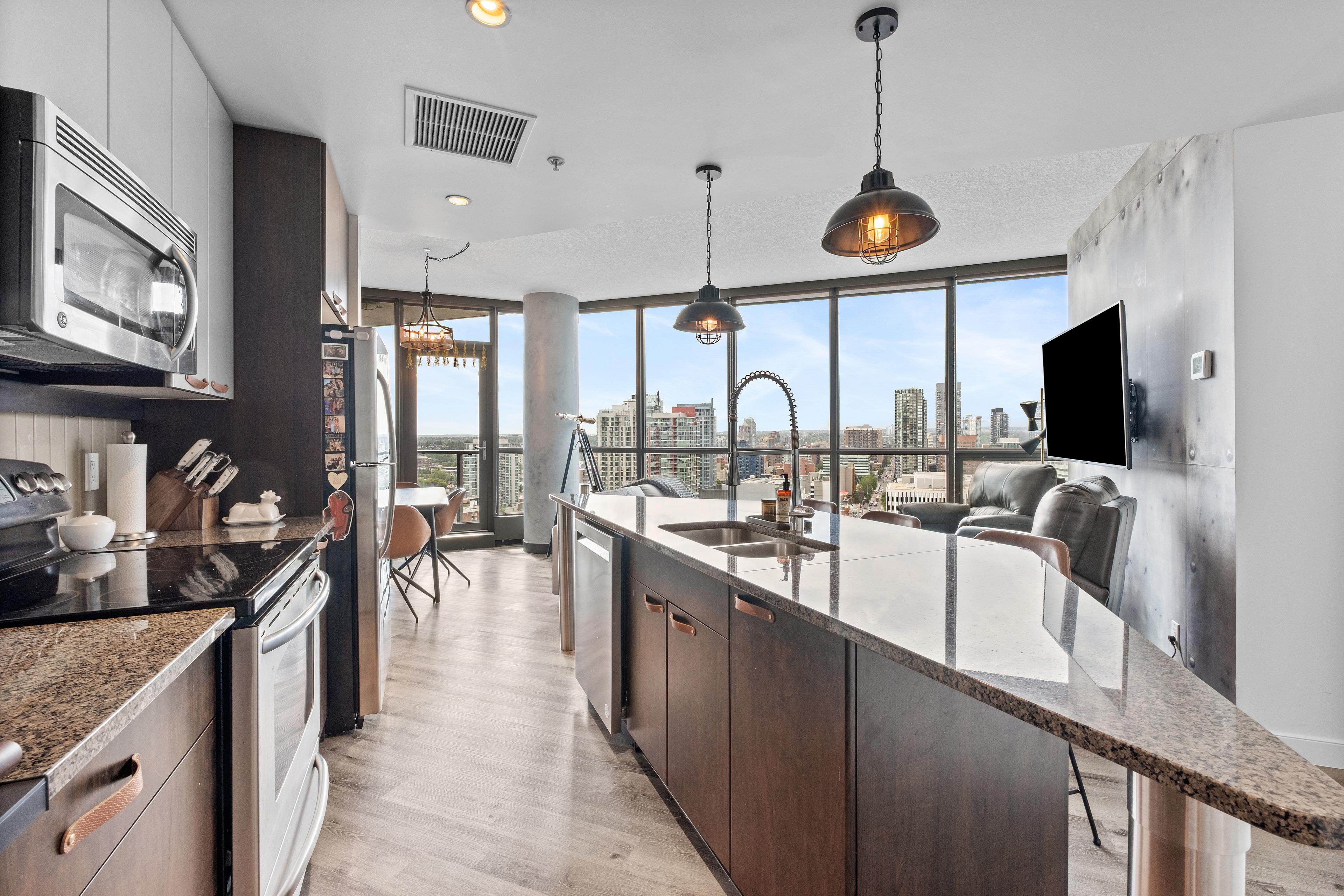 Condo kitchen with a granite island, pendant lights and city-view windows